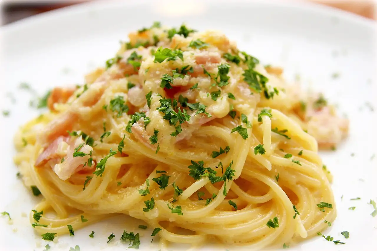 A white plate of spaghetti carbonara sprinkled with parsley and cheese