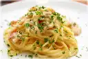 A white plate of spaghetti carbonara sprinkled with parsley and cheese