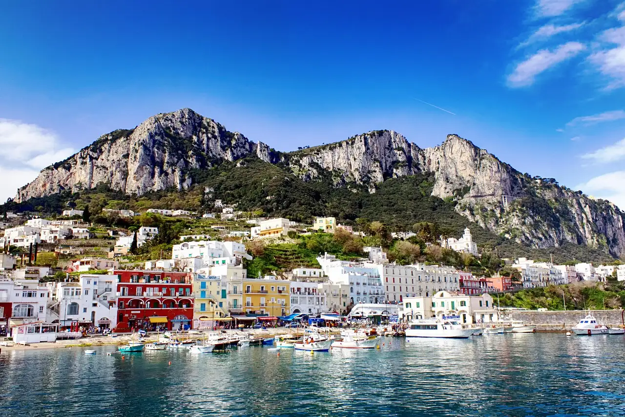 The harbor of Capri with boats, white houses and steep rocky hills behind
