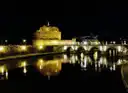Castel Sant'Angelo and its bridge lit up at night, reflected in the Tiber