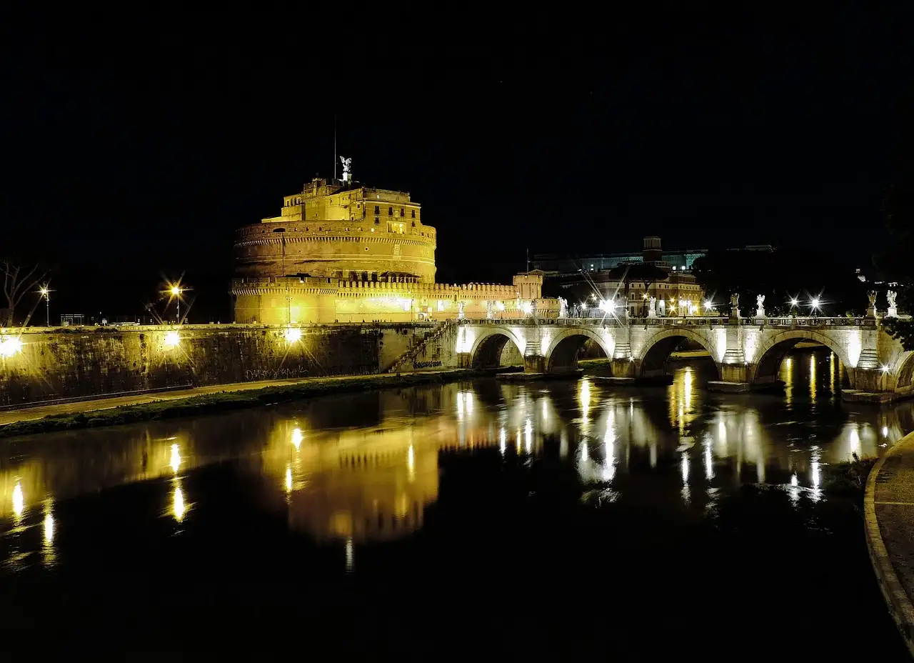 Castel Sant'Angelo and its bridge lit up at night, reflected in the Tiber