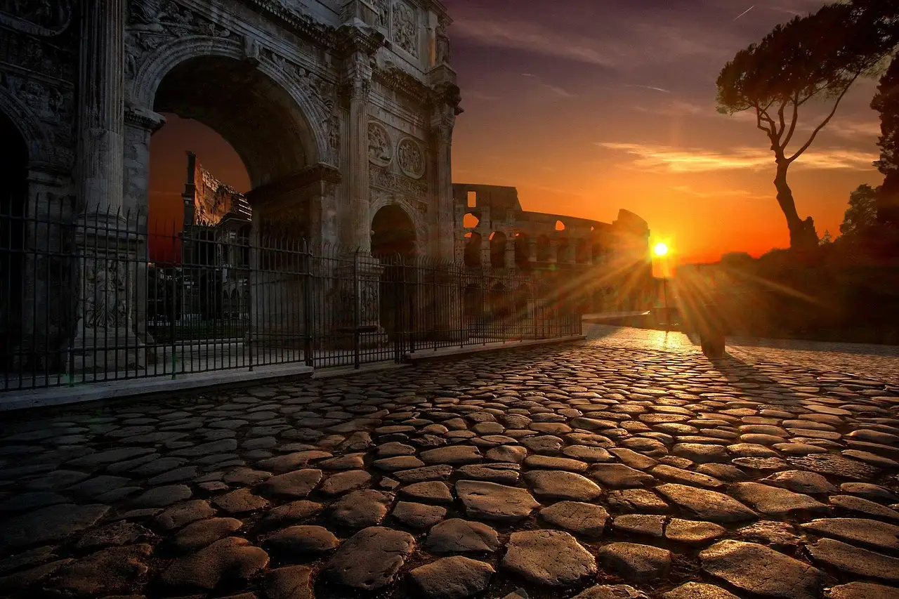 Sunset behind the Arch of Constantine and the Colosseum, seen along an old stone-paved road