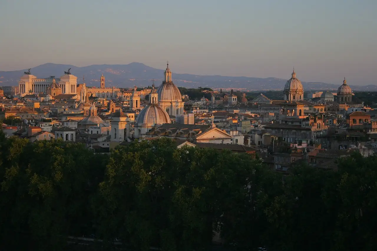Rome's domes and rooftops at sunset, with mountains on the horizon