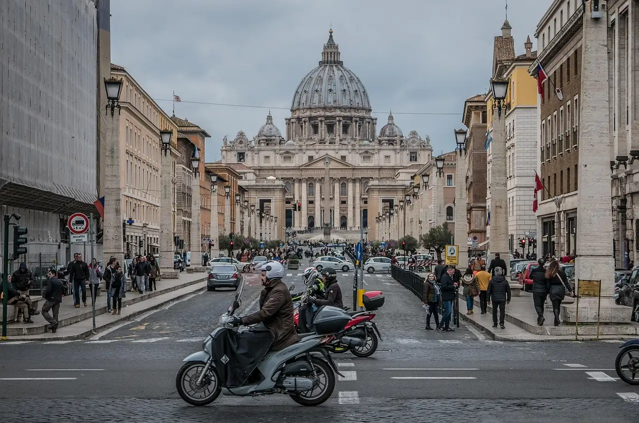 A busy Rome street with scooters and pedestrians, leading to St. Peter's Basilica