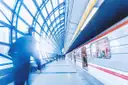 A blurred commuter walking along a glass-roofed metro platform beside a train
