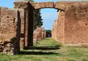 A grassy Roman street at Ostia Antica, lined with brick walls and an arch