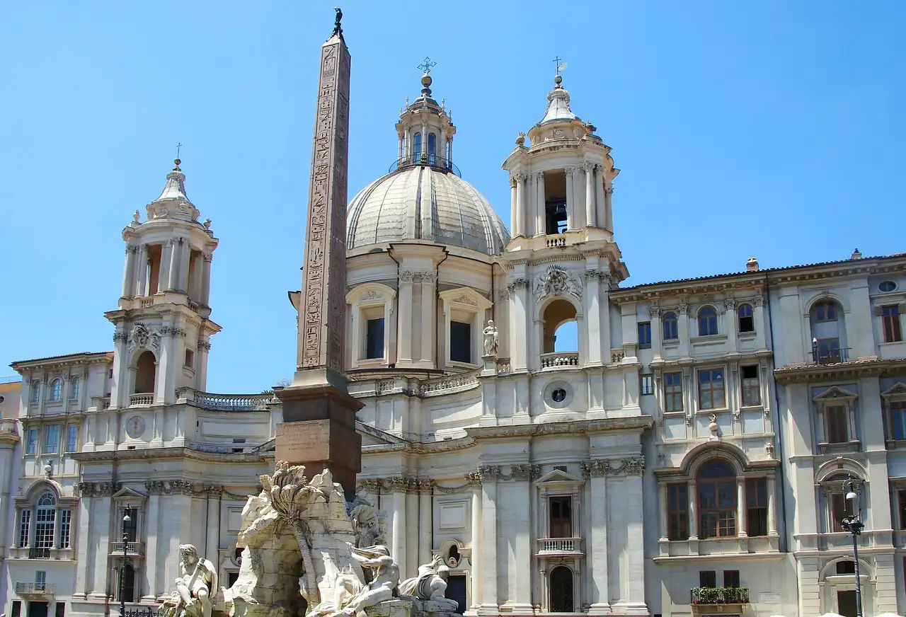 Piazza Navona with the obelisk, a fountain and the white church of Sant'Agnese in Agone under a blue sky