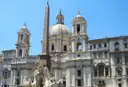 Piazza Navona with the obelisk, a fountain and the white church of Sant'Agnese in Agone under a blue sky