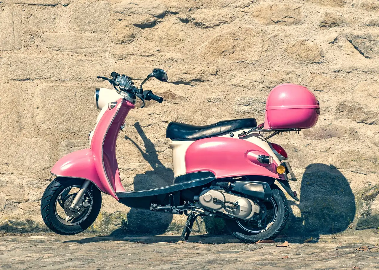A pink and cream scooter parked by a sunny stone wall