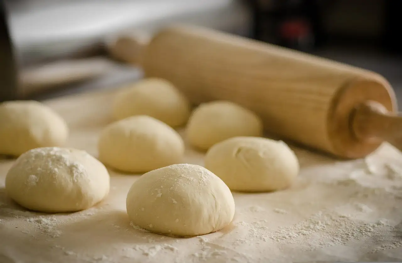 Balls of pizza dough on a floured table next to a rolling pin