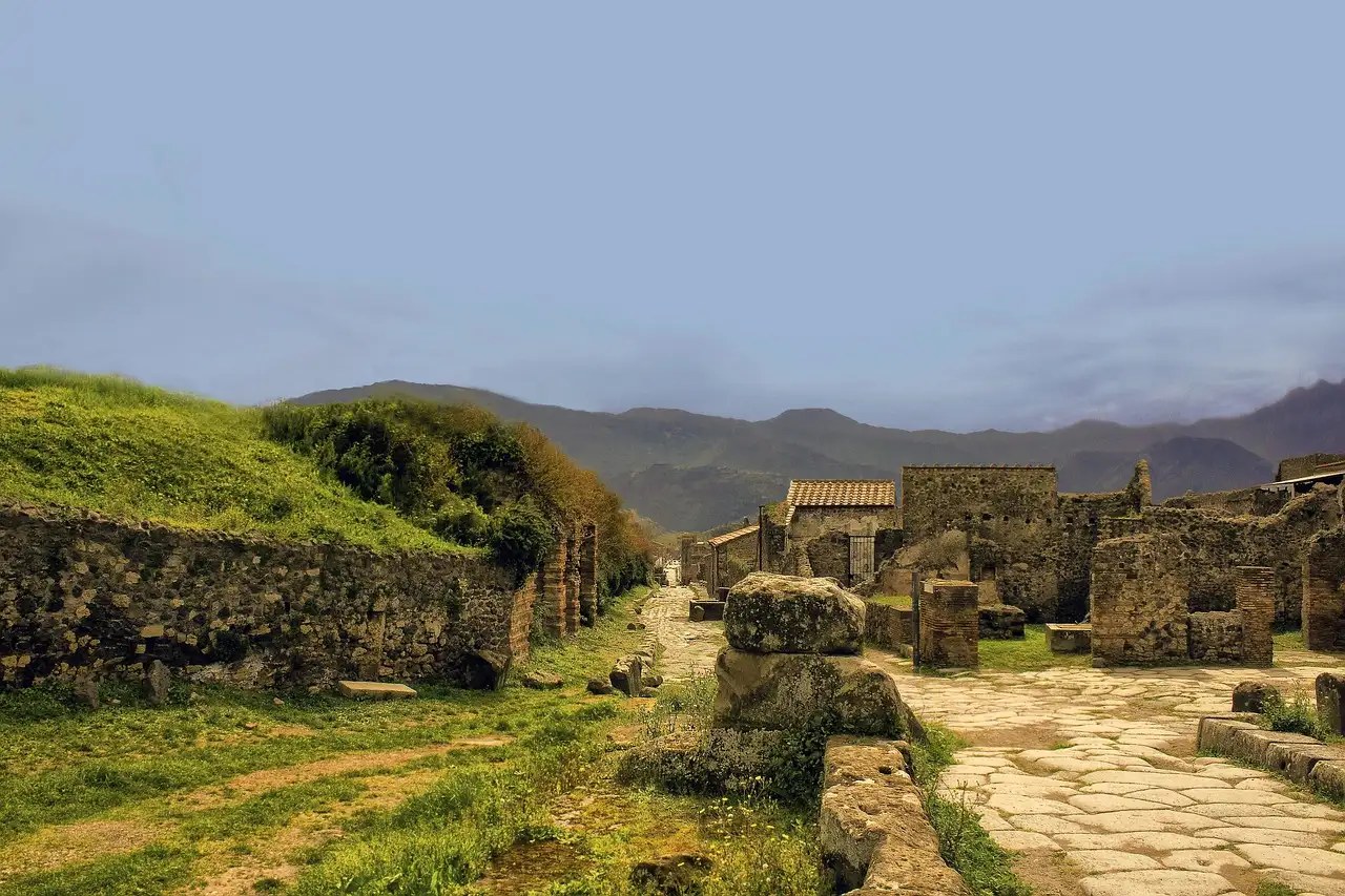 Low ruined walls and an old road in Pompeii, with green hills behind