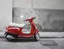 A red scooter parked by a grey wall on a stone street