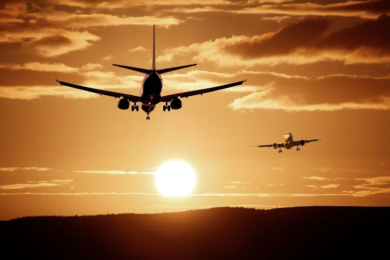 A passenger plane flying low at sunset with another plane in the distance
