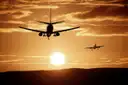 A passenger plane flying low at sunset with another plane in the distance
