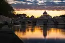 The Tiber and the dome of St. Peter's at sunset, with the river lit orange under scattered clouds