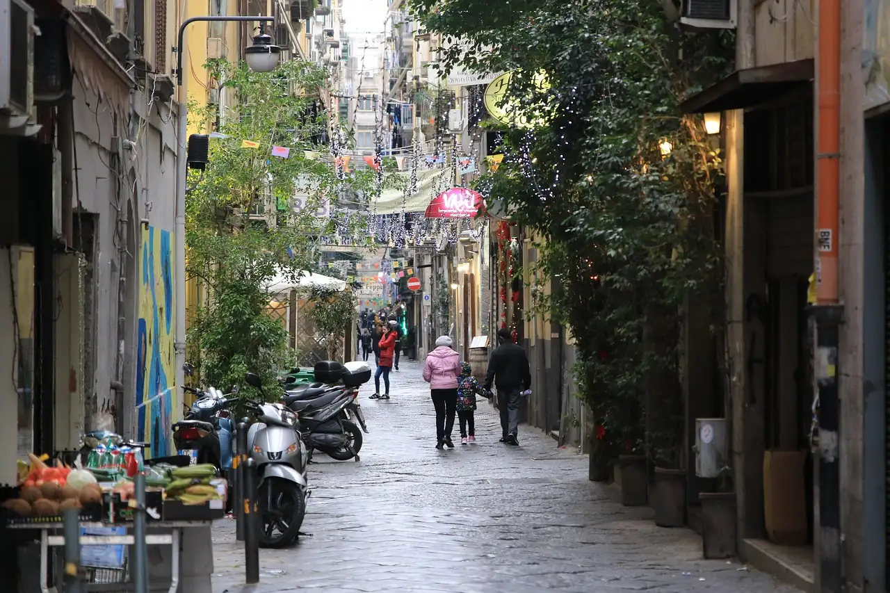 A narrow street in the old centre of Naples, with scooters, shops and people walking