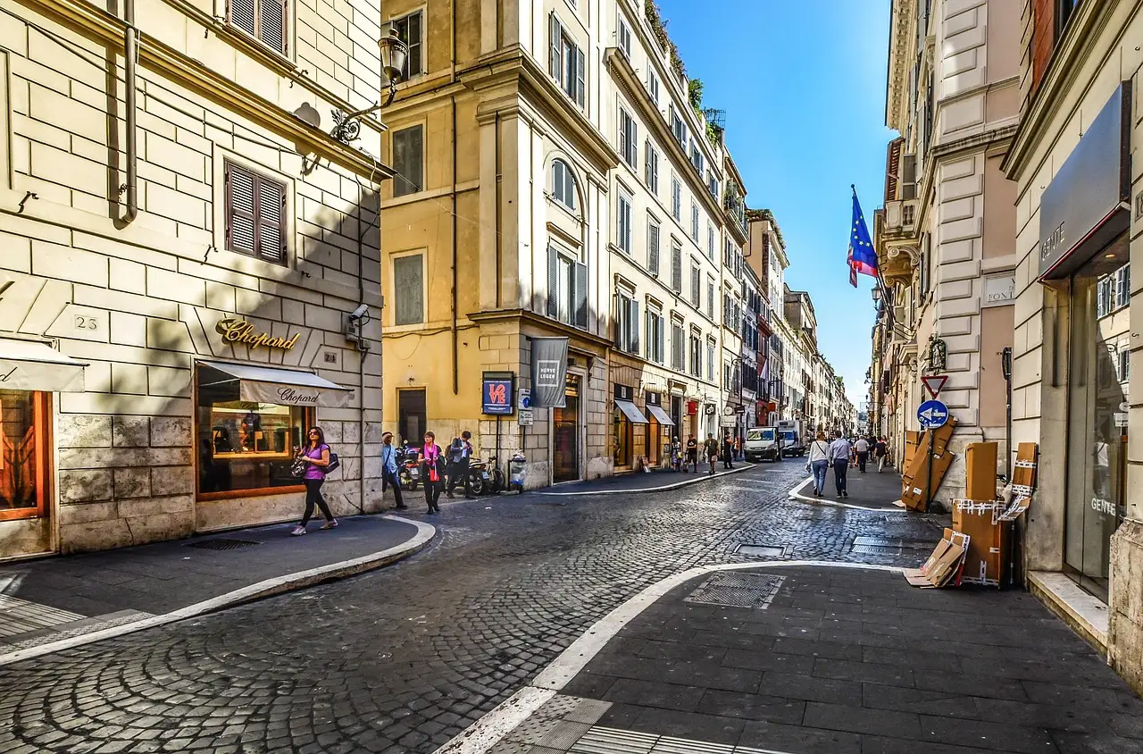 A cobbled shopping street in central Rome with shop windows and a few people walking