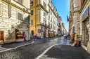 A cobbled shopping street in central Rome with shop windows and a few people walking