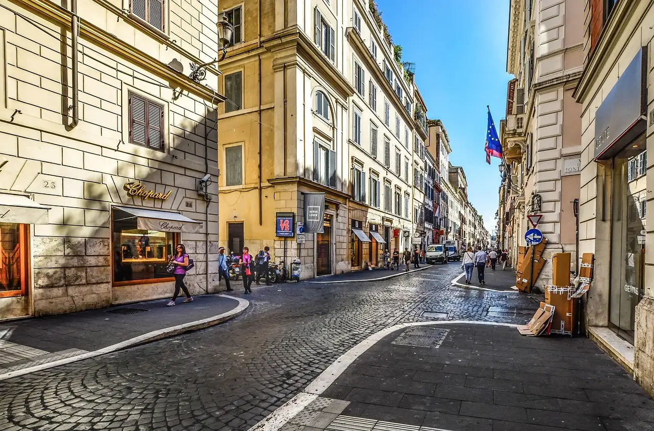 A cobbled shopping street in central Rome with shop windows and a few people walking