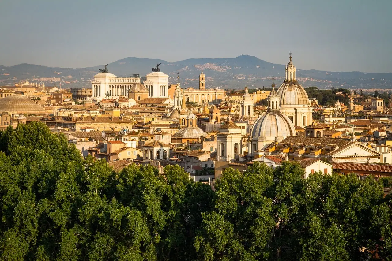 Rome rooftops and church domes in warm evening light, with hills far behind