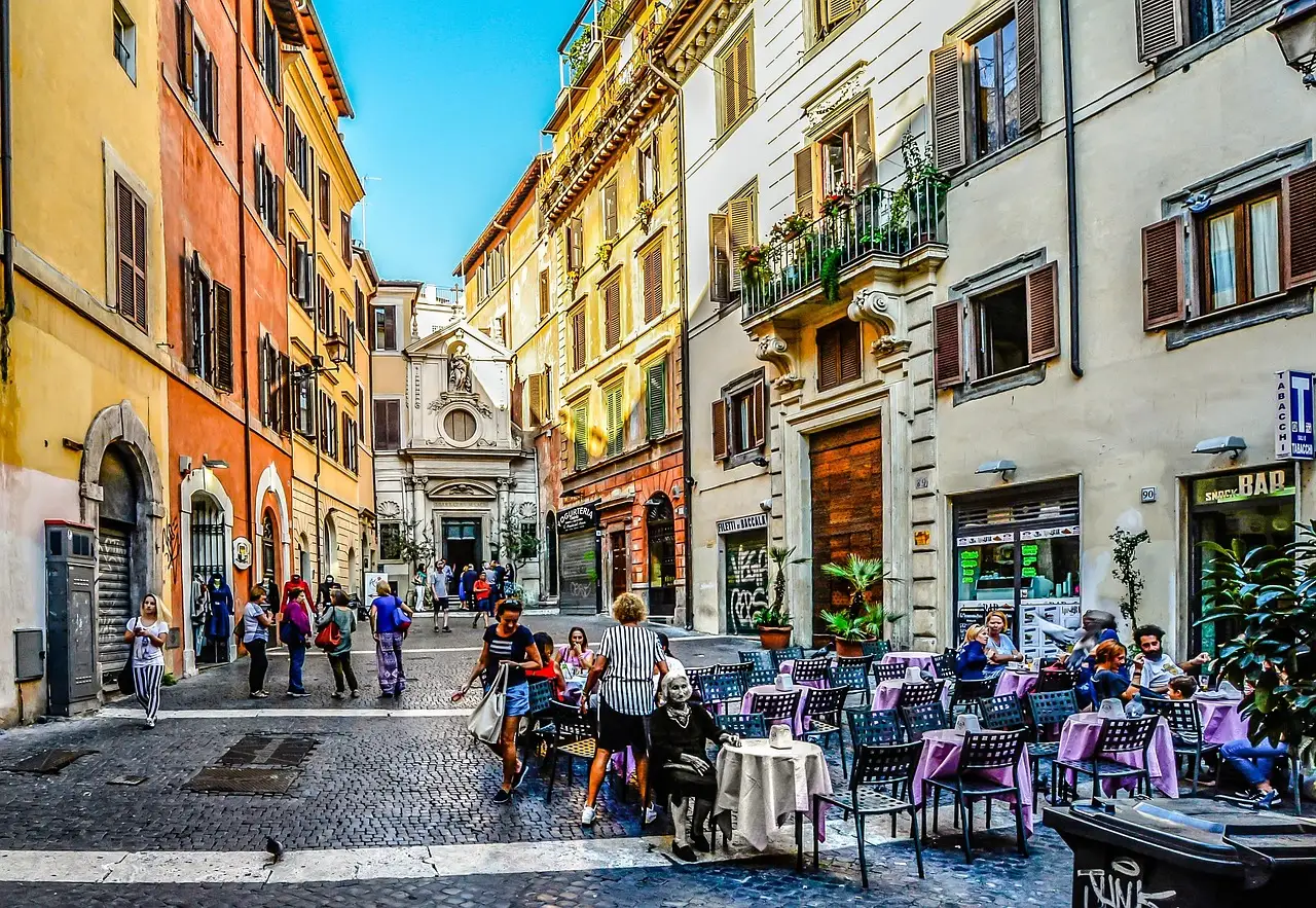 A cobbled Rome street with people sitting at café tables and colourful buildings