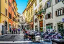 A cobbled Rome street with people sitting at café tables and colourful buildings