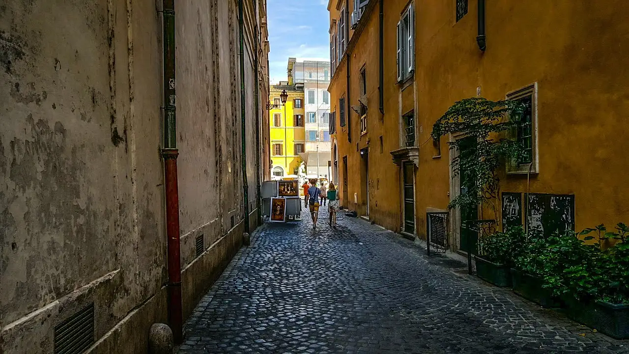 A quiet cobbled alley in Rome with ochre walls and a few people far away