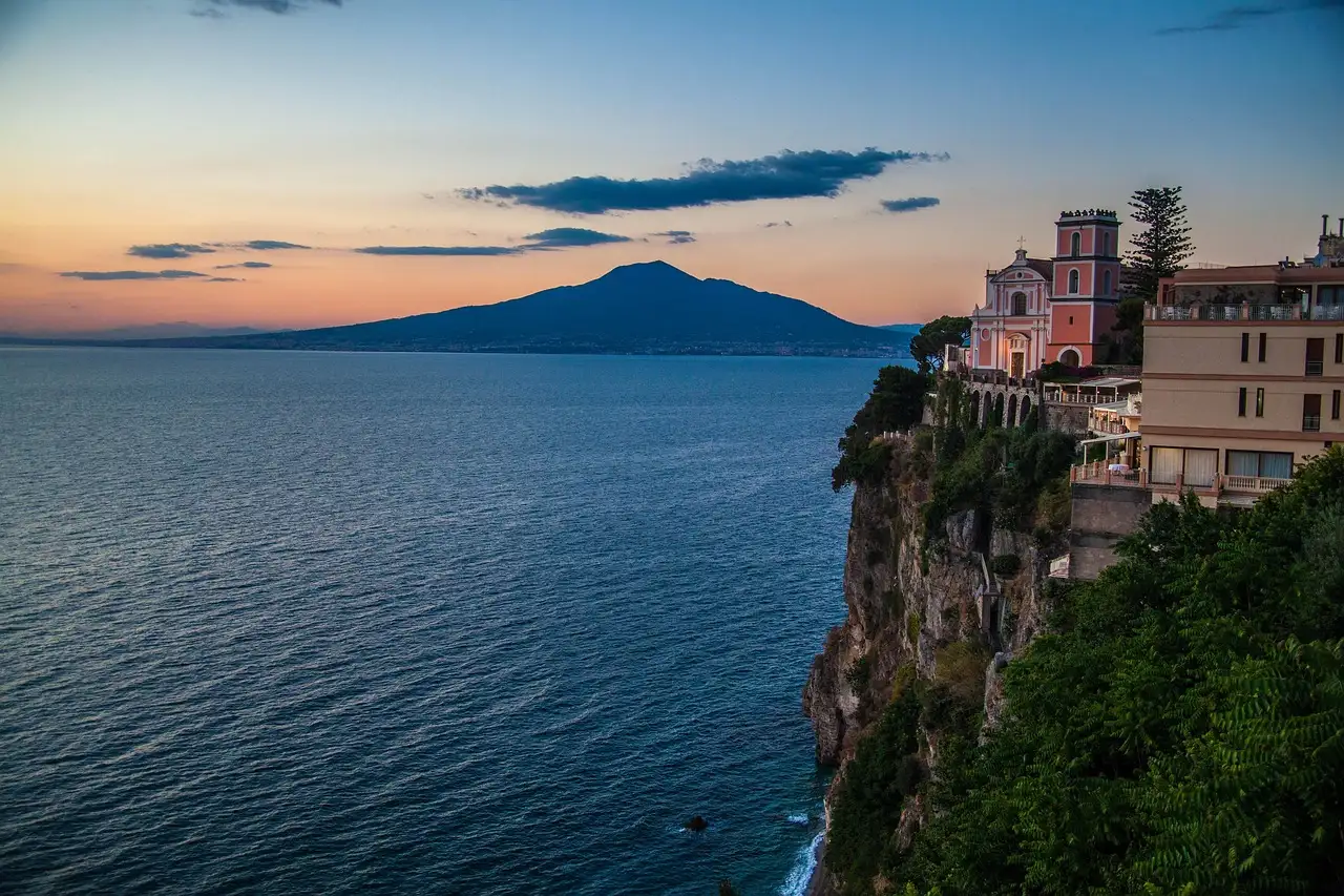 The cliffs of Sorrento above the sea at dusk, with Mount Vesuvius in the distance
