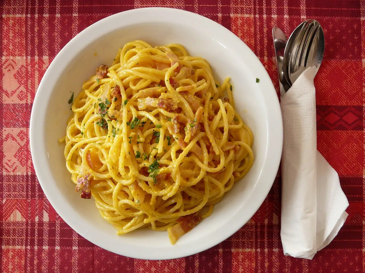 A plate of spaghetti carbonara on a red checked cloth