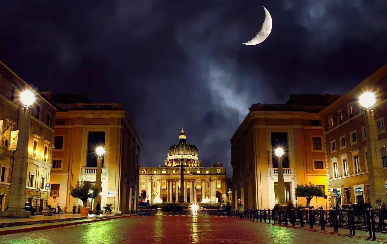 Via della Conciliazione and St. Peter's Basilica lit at night under a crescent moon