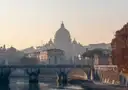 The dome of St. Peter's Basilica behind a bridge over the Tiber at sunset