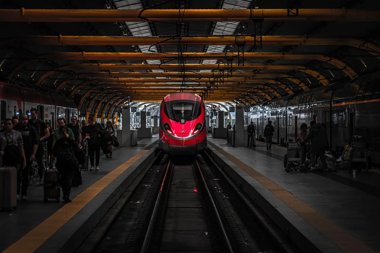 A red high-speed train arriving in a busy station hall with passengers on the platforms