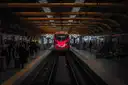 A red high-speed train arriving in a busy station hall with passengers on the platforms