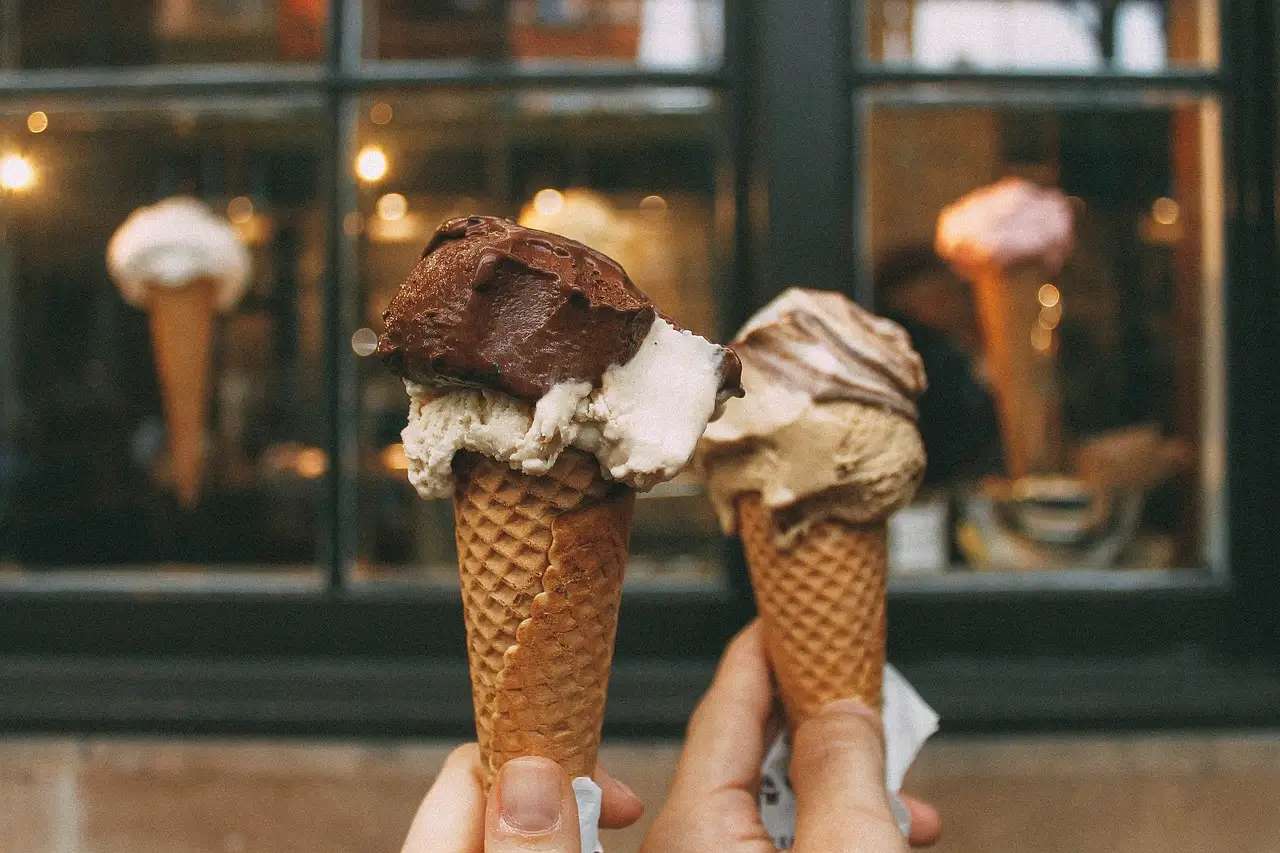 Two hands holding gelato cones in front of a gelato shop window