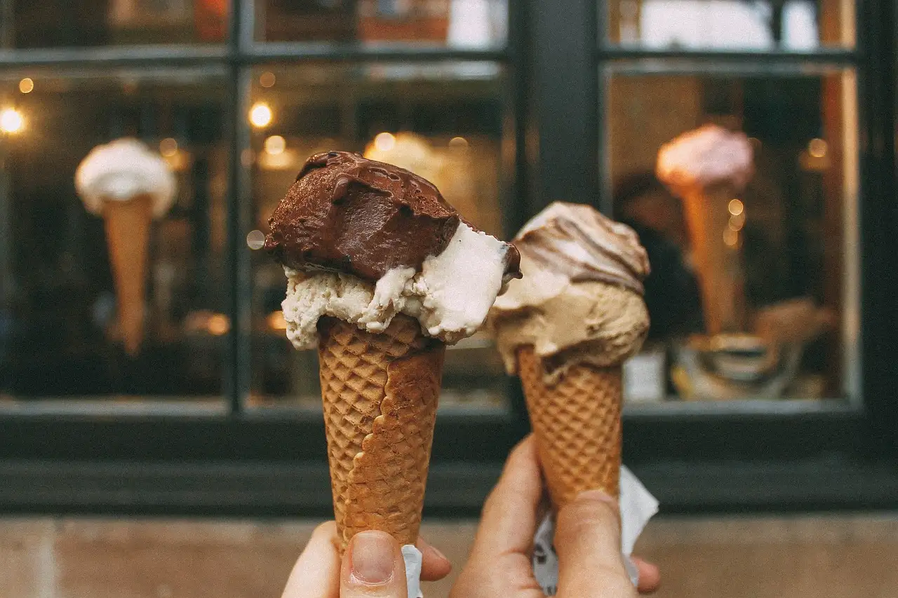 Two hands holding gelato cones in front of a gelato shop window