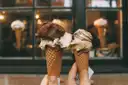 Two hands holding gelato cones in front of a gelato shop window