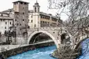 An old stone bridge over the Tiber with the buildings of Tiber Island