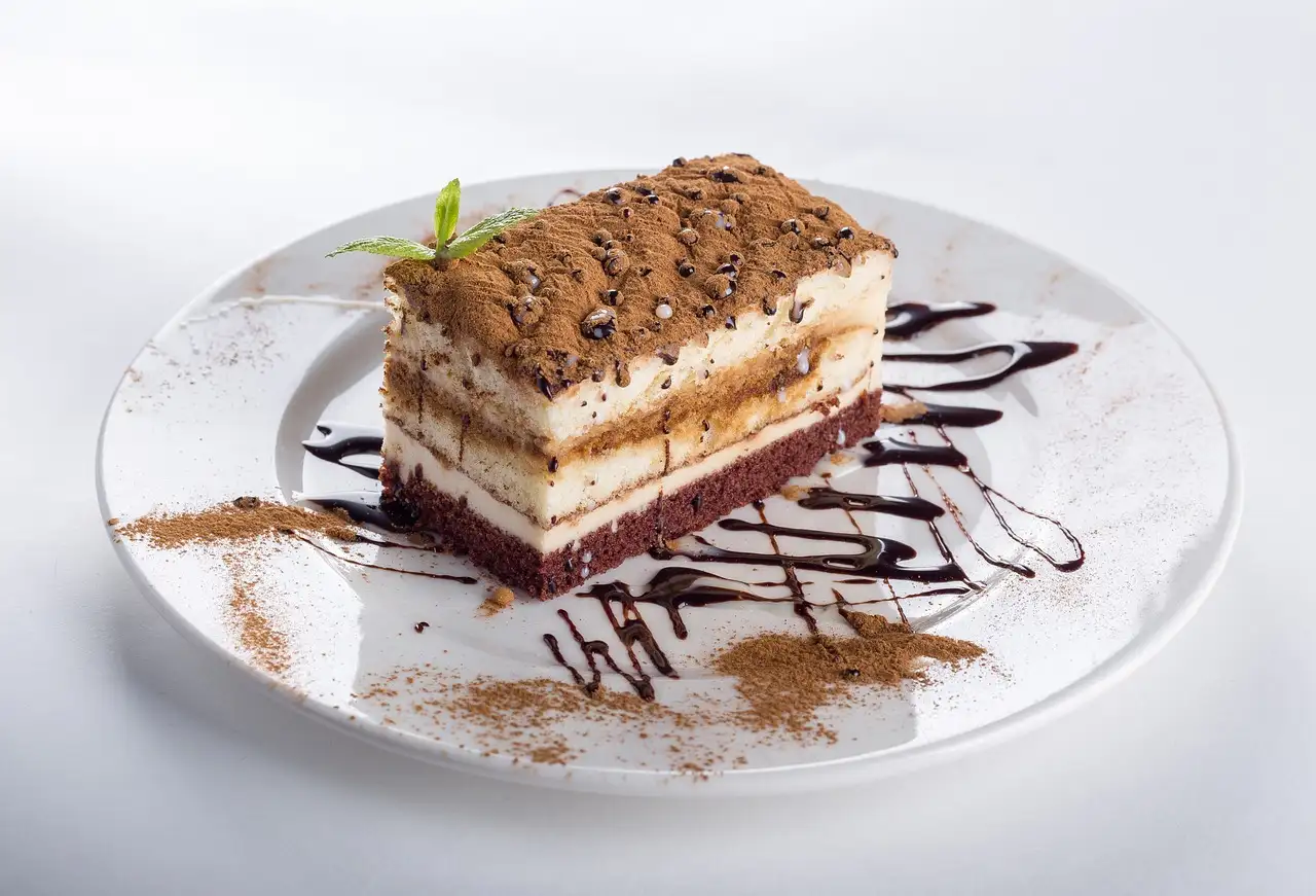 A slice of layered tiramisu dusted with cocoa on a white plate