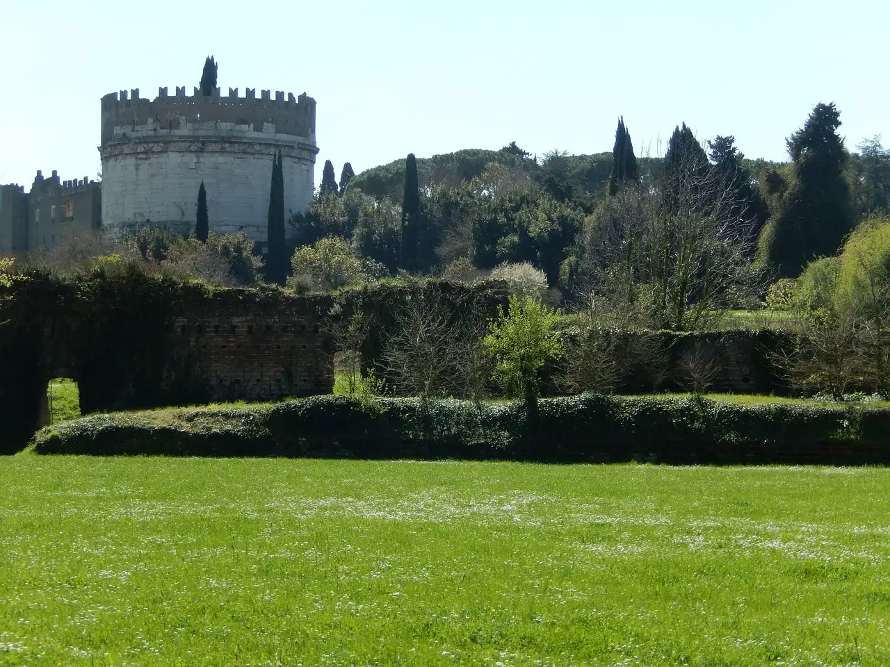 The round stone Tomb of Cecilia Metella on the Appian Way, behind a green lawn