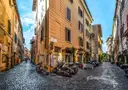 A cobbled lane in Trastevere with warm-colored houses and parked scooters