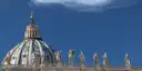 The dome of St. Peter's Basilica with statues along its roof under a deep blue sky