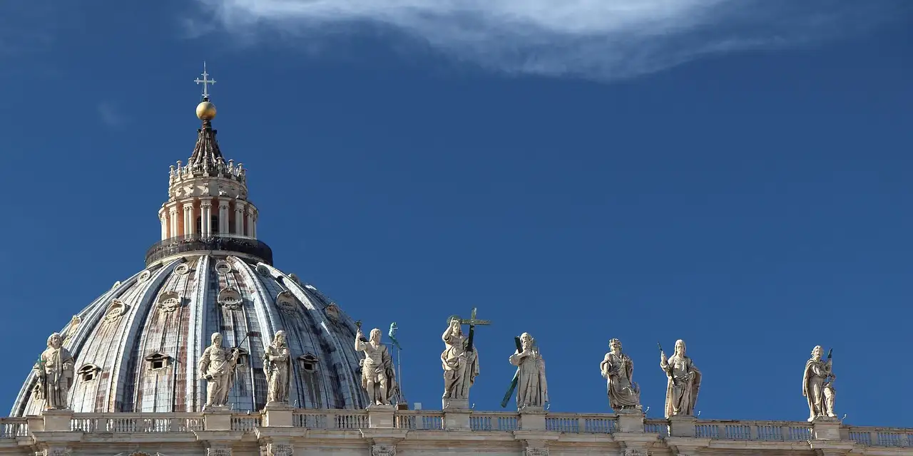 The dome of St. Peter's Basilica with statues along its roof under a deep blue sky